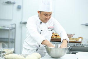 Chef in a white Richmond master baker uniform mixing ingredients in a metal bowl in a kitchen setting